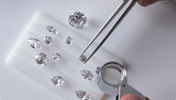 Pincettes ramassant un diamant dans un plateau contenant plusieurs diamants de tailles différentes