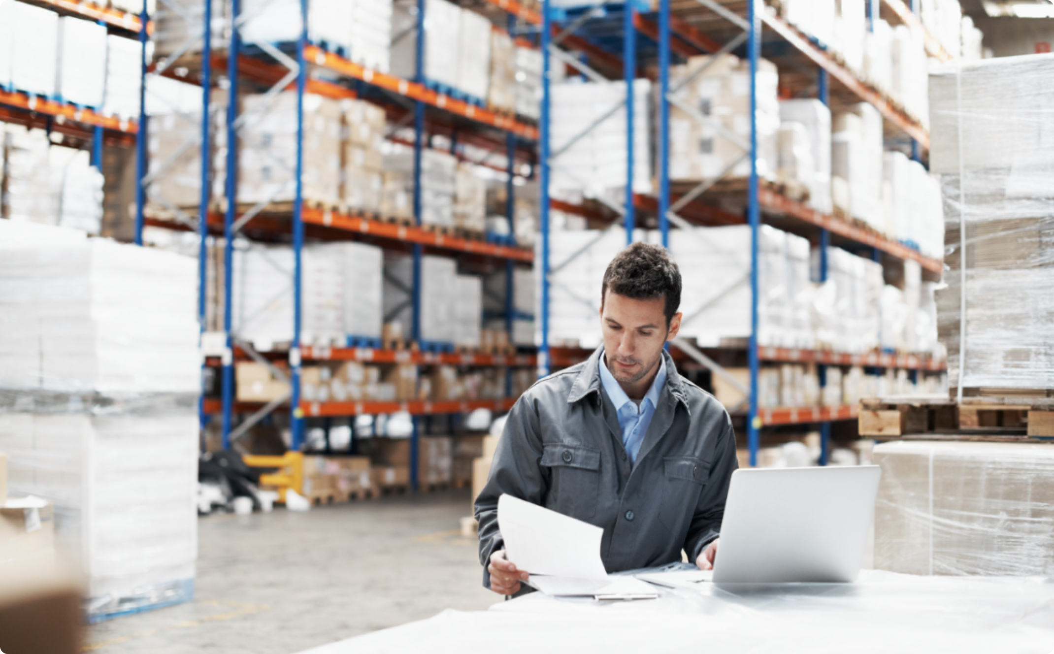 Male looking at a paper and working on a laptop in a warehouse