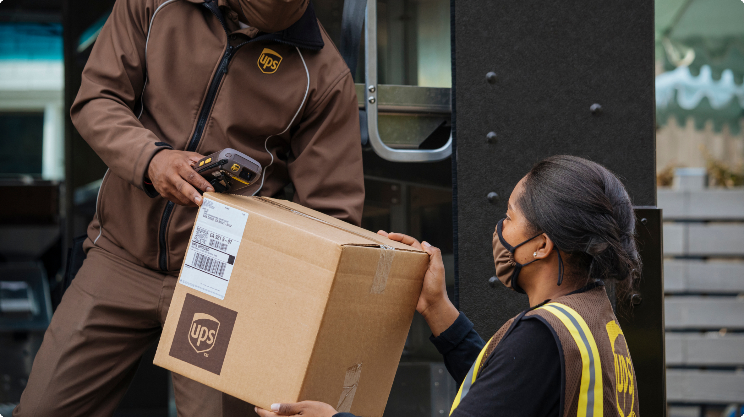  Male UPS worker handing a package from a truck to a female UPS worker